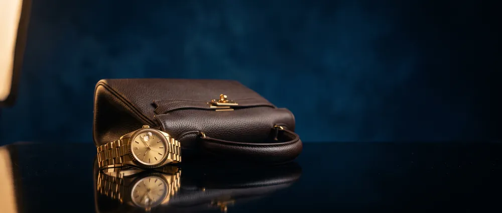 Orologio dorato e borsa in pelle su superficie lucida scura con luce di contorno